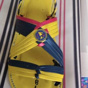 Bright yellow sandal with blue and pink crisscross straps and a circular emblem showing a world map on the strap.
