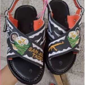 Pair of black open-toe sandals with orange interior and colorful embroidered patches on the straps, viewed from above on a pink background.